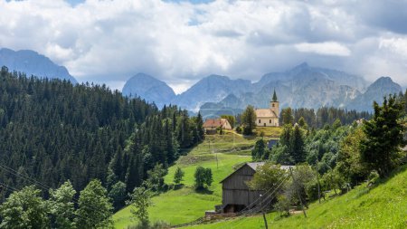 Church Cerkev Sveti Duh in Solava with mountain range Kamnik Savinja Alps in Slovenia on a sunny summer day.