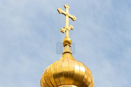 Die goldene Kuppel und das Kreuz der orthodoxen Kirche vor blauem Himmel und Wolken.