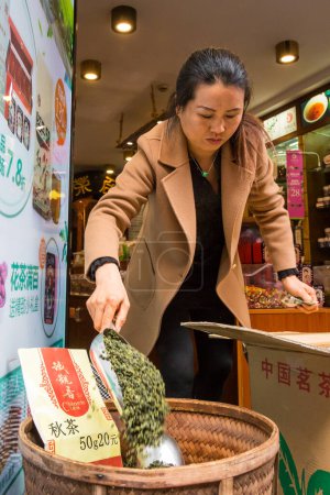 Photo for Female business owner stands in front of small market store filling tea bins in the Water Town Bazaar in Zhujiajiao in the Qingpu District of Shanghai China April 04, 2017 during the celebration of the Tomb Sweeping Day national holiday. - Royalty Free Image