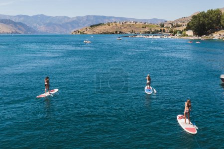Photo for A sunlit holiday on the water at Lake Chelan with a group of people paddle boarding. Pacific Northwest Washington State - Royalty Free Image