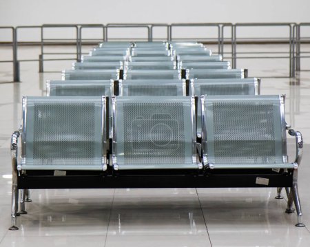Photo d'un trois personnes chrome poli robuste, acier inoxydable, chrome, aluminium et des chaises de fer avec des poignées dans un espace public intérieur dans une rangée avec des barrières métalliques en arrière-plan. Pas de peuple