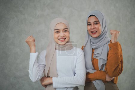 Téléchargez les photos : Deux femmes islamiques asiatiques portant des robes formelles et foulards hijab se tiennent avec leurs bras croisés souriant avec confiance et convivialité en regardant la caméra. - en image libre de droit