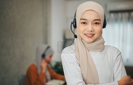 Téléchargez les photos : Femme musulmane portant un foulard en hijab et un casque debout à l'intérieur du bureau, concept de service après-vente, télévente et employés fournissent des informations en ligne. - en image libre de droit