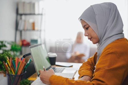 Téléchargez les photos : Femme islamique portant hijab foulard étudier en ligne avec ordinateur portable à la maison. - en image libre de droit