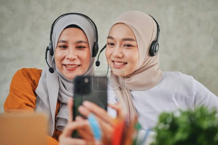 Téléchargez les photos : Réceptionniste islamique et femme du service d'information portant un casque prenant des photos avec des smartphones. - en image libre de droit