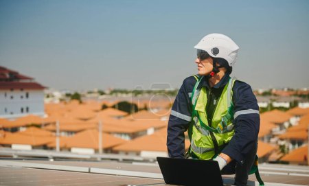 Téléchargez les photos : Ingénieur portant un équipement de protection pour travailler en hauteur installant un système de production d'énergie solaire sur le toit d'un bâtiment d'usine. - en image libre de droit