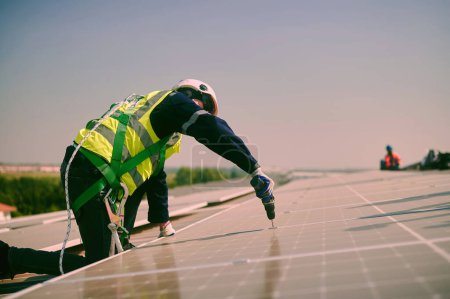 Téléchargez les photos : Skilled solar panel installers wearing protective gear and helmets are doing installation work on the roof. - en image libre de droit
