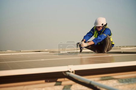 Téléchargez les photos : Ingénieur portant un équipement de protection pour travailler en hauteur installant un système de production d'énergie solaire sur le toit d'un bâtiment d'usine. - en image libre de droit