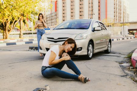 Asian woman was hit by a car while crossing the road and sitting on the floor injured legs and knees. Walking knee pain unable to walk with painful face : Female driver looked shocked and guilty.
