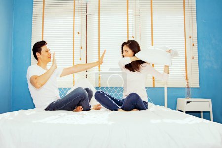 Foto de Juguetonas parejas asiáticas usan peleas de almohadas en sus colchones porque resienten algo que los hombres no se complacen y hacen como su novia ordena para hacer que las mujeres estúpidas peleen pero los hombres se rinden. - Imagen libre de derechos