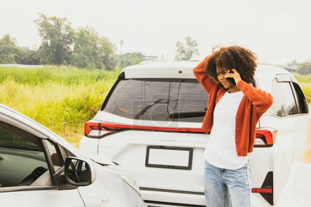 Téléchargez les photos : Femme afro-américaine frustrée regarde sa propre voiture sur la route qui a été frappé et l'arrière de la voiture est endommagé à l'aide d'un smartphone pour dire à la compagnie d'assurance pour effacer et évaluer les dommages. - en image libre de droit