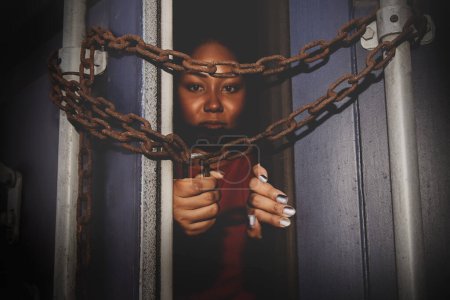 Téléchargez les photos : African American woman trapped in an illegal cargo container locked with chains and keys. Has the idea of trying to escape and seeking freedom from the outside : Concept of human trafficking - en image libre de droit