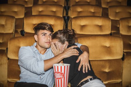 Téléchargez les photos : Couple caucasien regardant un film d'horreur effrayant dans un cinéma multiplex, choquant leurs copines, n'osent pas regarder, ne peuvent que les embrasser et les protéger en toute sécurité dans une étreinte romantique chaude. - en image libre de droit
