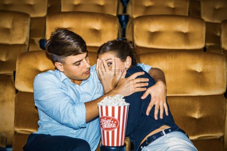 Téléchargez les photos : Couple caucasien regarder film d'horreur effrayant cinéma multiplex choquant leurs copines n'osent pas regarder ne peut que câliner avec amour et chérir et les protéger en toute sécurité dans une étreinte romantique chaude. - en image libre de droit