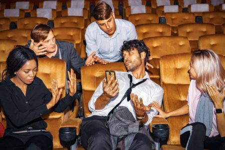 Photo for Concept Etiquette in the cinema Do not talk on the phone to disturb others : Man who is talking on the phone among moviegoers is annoying those around him who are upset for bad behavior. - Royalty Free Image