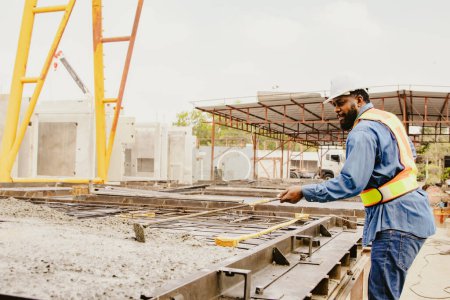 Afroamerikanischer Vorarbeiter mit einem Werkzeug, um den Zement in Fertigteilen gleichmäßig einzuebnen, während er den Zement auf die Baustelle gießt.