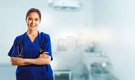 Photo for Portrait female Thai surgeon in blue uniform with stethoscope standing crossed hands smiling looking at camera friendly to everyone standing smart in operating room : Copy Space - Royalty Free Image