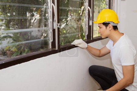 Photo for Male staff, Asian termite exterminators wearing hard hats inspecting old wooden window sills to detect termite nests, insects and areas where termites cause housing problems to eliminate and prevent. - Royalty Free Image