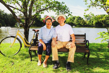 Photo for Senior asian retired couple healthy and cheerful travel health park parking bicycle sitting bench in an outdoor garden clear weather next shady pond looking at the beauty inside the amazing garden. - Royalty Free Image