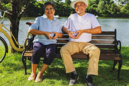 Seniorenpaar zeigt Herz-Design-Symbol mit Händen zusammen: Seelenverwandte, lange glückliche Liebeshochzeit, glückliche Momente beim Zusammensitzen im Vorgarten.