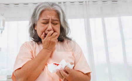 Foto de Ancianos mujer asiática estresada, llorar preocupación sentado en una cama hospital sala de emergencias que sufren de neumonía tos que la puso en riesgo de cáncer de pulmón se sorprendió al ver la sangre en su esputo. - Imagen libre de derechos