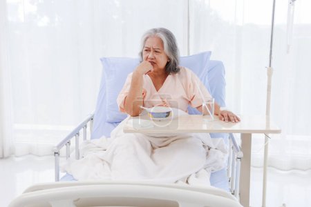 Foto de Mujer asiática anciana, paciente con gastritis, enfermedad gastrointestinal, hospitalizada, cansada de comer sosa, papilla desagradable, no tiene apetito. No quiero comer, estoy cansado de recuperarme.. - Imagen libre de derechos