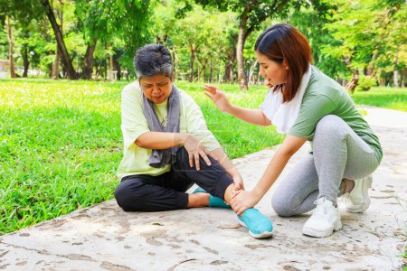 Ältere Frau sitzt mit Schmerzen im linken Knöchel beim Joggen im Garten und erhält von ihrer Tochter Erste Hilfe wegen verstauchter Knöchelschmerzen mit Vorsicht: Ältere Gesundheit in der Versicherung.