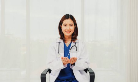 Téléchargez les photos : Femme médecin chirurgien bénévole en uniforme blanc avec stéthoscope médical doux siège dans le bureau détend souriant à la caméra amical donnant de bons voeux de bonheur à tout le monde. - en image libre de droit