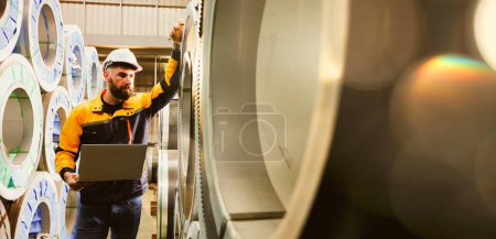 Male technician inspects stock in the raw material storage area steel coils large rolls metal sheets high quality strong durable standard within industrial factory product production metal sheet roof.