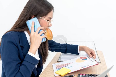 Foto de Asian business woman busy with work, where she eats while working because she hastened to complete the work according to the goal, to business and work so busy that you don't have time to eat concept - Imagen libre de derechos