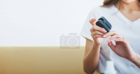 Foto de Asian woman sitting on the sofa, checking her health by using the oxygen level measuring device, with white background, to people and health care concept. - Imagen libre de derechos