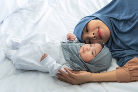 Foto de La familia musulmana, la atractiva madre asiática y la niña recién nacida de 2 meses, es mitad nigeriana mitad tailandesa, relajada y acostada en una cama blanca. a la relación en la familia islámica y concepto de bebé. - Imagen libre de derechos