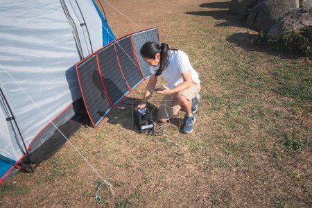 Téléchargez les photos : Touristes asiatiques de camping masculin, recharge batterie de téléphone de Power Box. qui reçoit de l'énergie du panneau solaire, qui reçoit de l'énergie du soleil. au concept de voyage et camping. - en image libre de droit