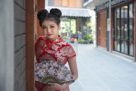 Foto de Chica asiática con un cheongsam rojo sostiene un ventilador de madera en su mano. Pose para fotos en Chinatown Según la idea de Año Nuevo Chino - Imagen libre de derechos