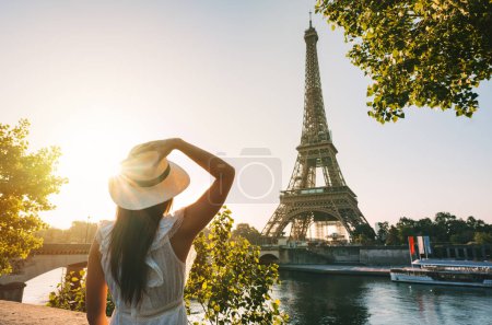 Foto de Joven turista con sombrero de sol y vestido blanco de pie frente a la Torre Eiffel en París al atardecer. Viajar en Francia, concepto de turismo. Foto de alta calidad - Imagen libre de derechos