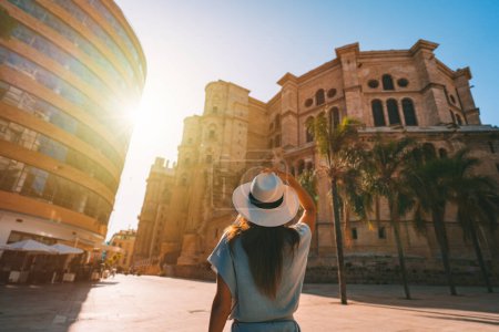 Vue arrière de la jeune touriste en chapeau de soleil blanc marchant dans la ville de Malaga au coucher du soleil. Vacances d'été en Espagne. Photo de haute qualité