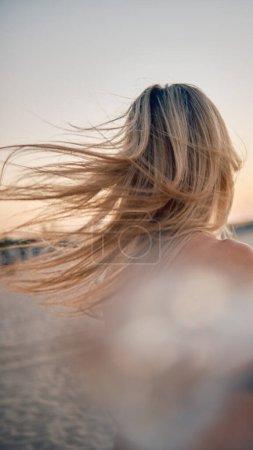 Photo for An evocative scene with a blonde woman's windswept hair by the seaside at golden hour capturing movement and natural beauty - Royalty Free Image