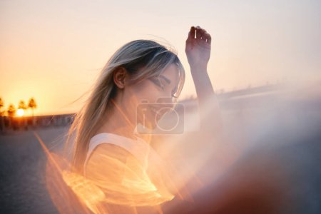 Contra una puesta de sol de enfoque suave, la silueta de una mujer levanta la mano en un gesto pacífico, evocando una sensación de serenidad y reflexión