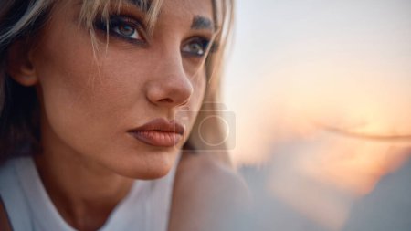 Eine nachdenkliche und emotional eindrucksvolle Nahaufnahme des Gesichts einer Frau vor dem Hintergrund eines Sonnenuntergangs