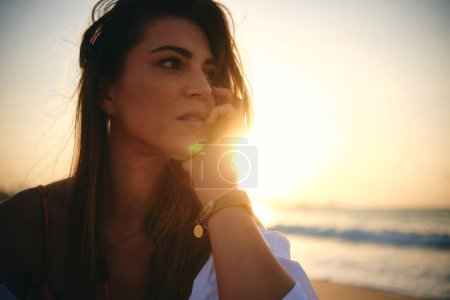Eine ruhige Frau am Strand während des Sonnenuntergangs, ihr Gesicht teilweise von einer Linse beleuchtet