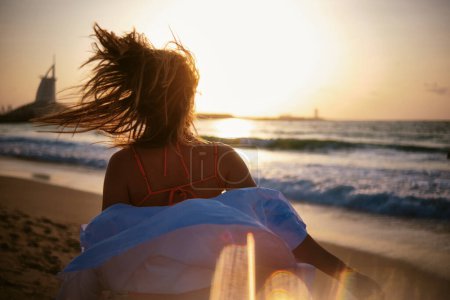 Femme regarde vers la mer avec le vent soufflant ses cheveux, avec le Burj Al Arab au loin