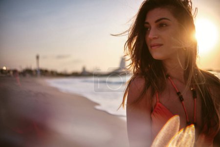 Foto de Primer plano de una atractiva mujer sonriendo suavemente con la playa de iluminación al atardecer en el fondo - Imagen libre de derechos