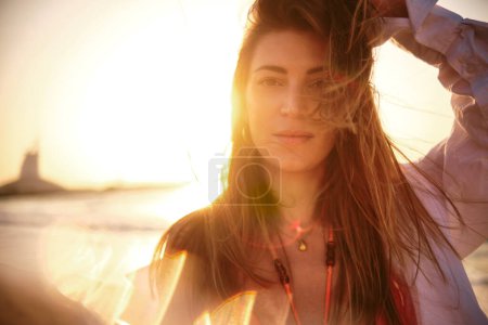 Frau mit wehenden Haaren, die gegen den Sonnenuntergang steht und einen Leuchteffekt erzeugt