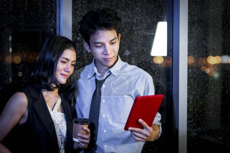 Photo for Happy smiling Asian business man and woman working together, look at digital tablet and have discussion, employee working hard overtime at night in office, hard-working officer colleague work overnight - Royalty Free Image