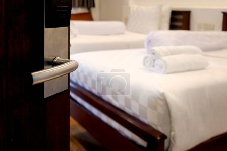 Opened door with blurred background of stack of fresh white bath towels on white bed in hotel room, travel and convenient relaxation at hotel concept.