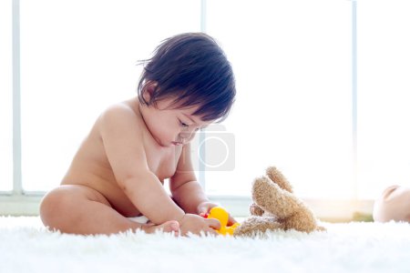 Photo for Happy toddle baby kid sitting on fluffy white rug floor in living room, little girl daughter playing with toys, cute infant child at home, love in family, childhood and baby care. - Royalty Free Image