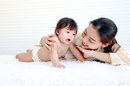 Photo for Portrait of happy toddle baby lying on fluffy white rug with mother, little cute kid girl tries to crawl, mom hugs her daughter child, love in family, childhood and motherhood concept. - Royalty Free Image