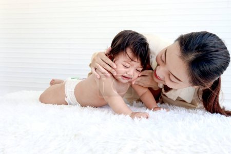 Photo for Portrait of happy toddle baby lying on fluffy white rug with mother, little cute kid girl tries to crawl, mom hugs her daughter child, love in family, childhood and motherhood concept. - Royalty Free Image