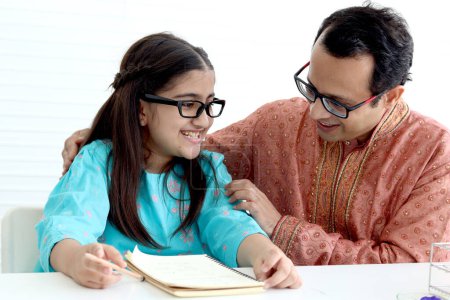 Photo for Cute Indian school student girl in traditional dress and glasses do homework with father, father teaching daughter kid at home, parent become teacher tutor involvement in childhood education in family - Royalty Free Image