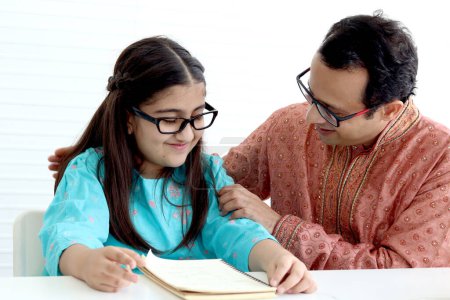 Photo for Cute Indian school student girl in traditional dress and glasses do homework with father, father teaching daughter kid at home, parent become teacher tutor involvement in childhood education in family - Royalty Free Image